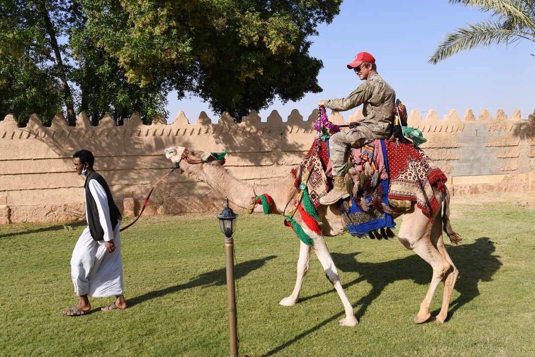 A service member rides a camel.