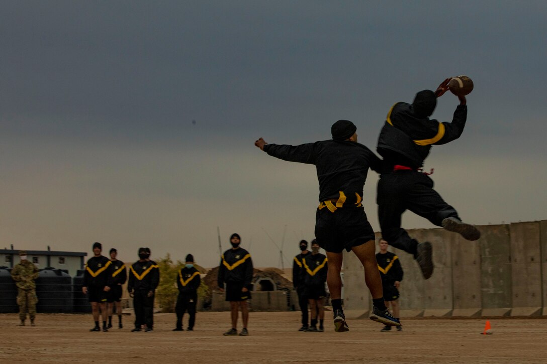 A soldier jumps to catch a football as other service members watch.