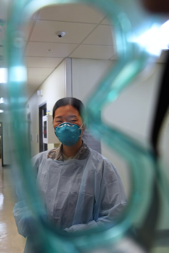 U.S. Air Force Airman 1st Class Angelina Lee, 17th Healthcare Operations Squadron aerospace medical technician, dons COVID-19 protective equipment prior to screening a patient at the Ross Clinic on Goodfellow Air Force Base, Texas, Nov. 23, 2020. Lee wore a mask and gown, and would put on goggles to avoid possible contact contamination with COVID-19. (U.S. Air Force photo by Senior Airman Abbey Rieves)