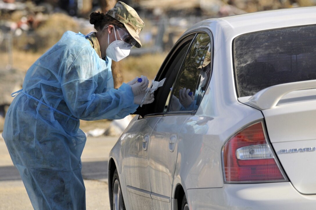 A guardsmen wearing personal protective equipment administers a COVID-19 test to a person in a vehicle.