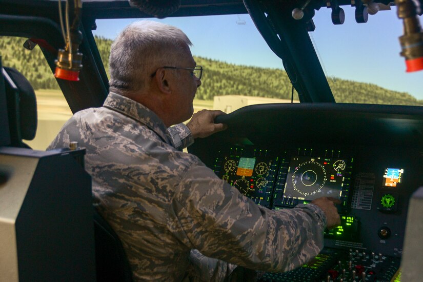 A man in a military uniform sits inside a simulated aircraft cockpit.