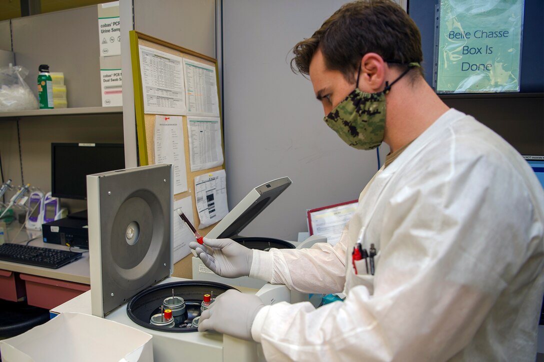 A sailor wearing personal protective equipment prepares a blood sample for testing.
