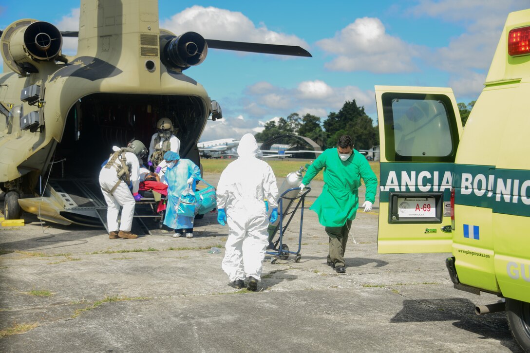 Soldiers wearing personal protective equipment carry a COVID-19 patient out of a CH-47 Chinook.