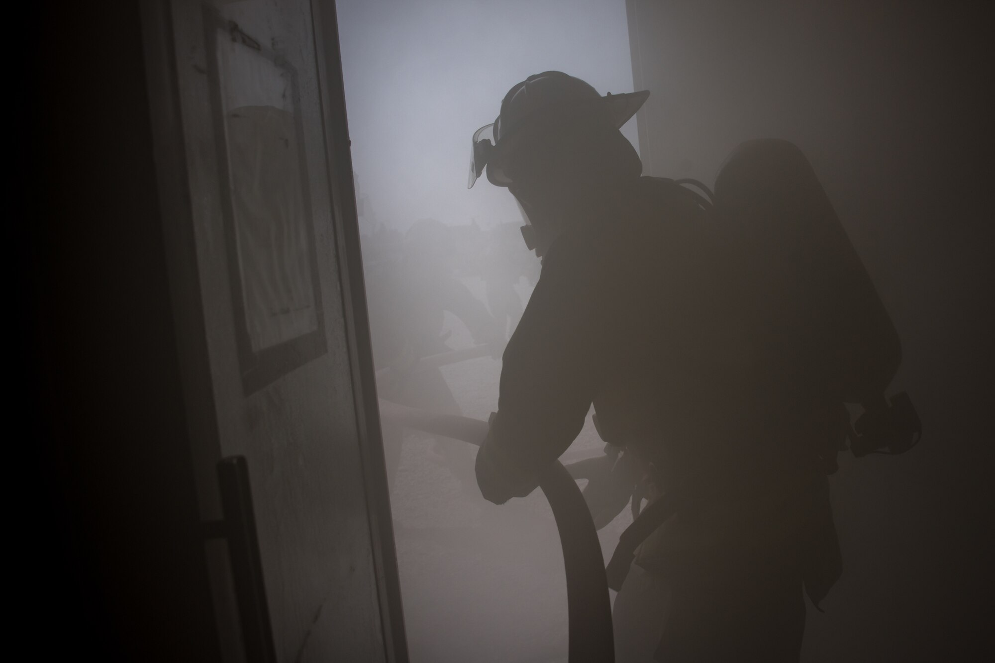 firefighter pulls a hose into a building full of smoke from a smoke machine