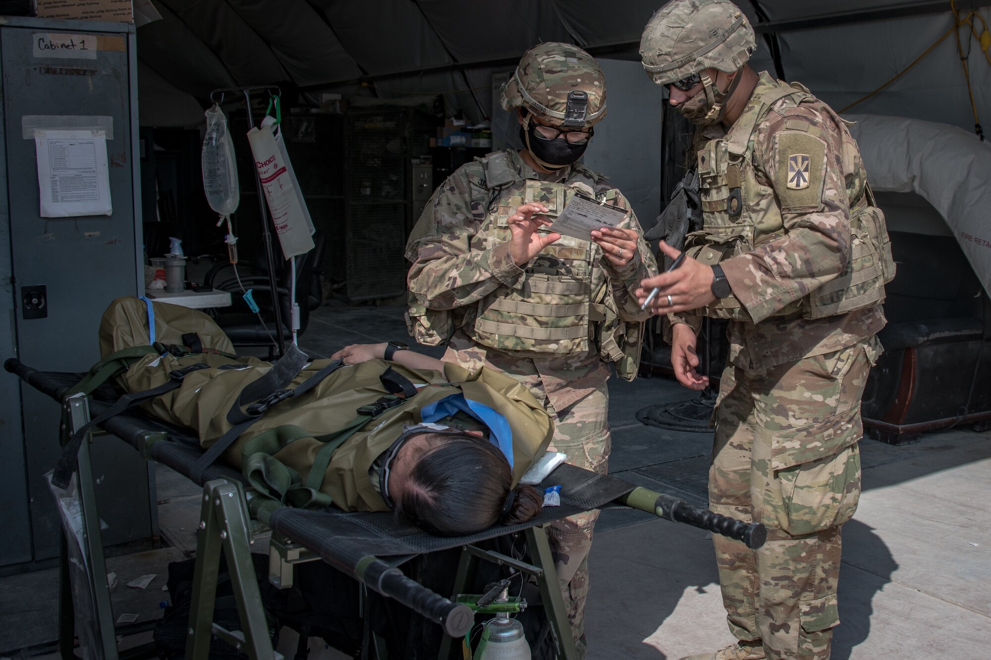 two U.S. soldiers look at a card with vitals of a simulated patient marked on it