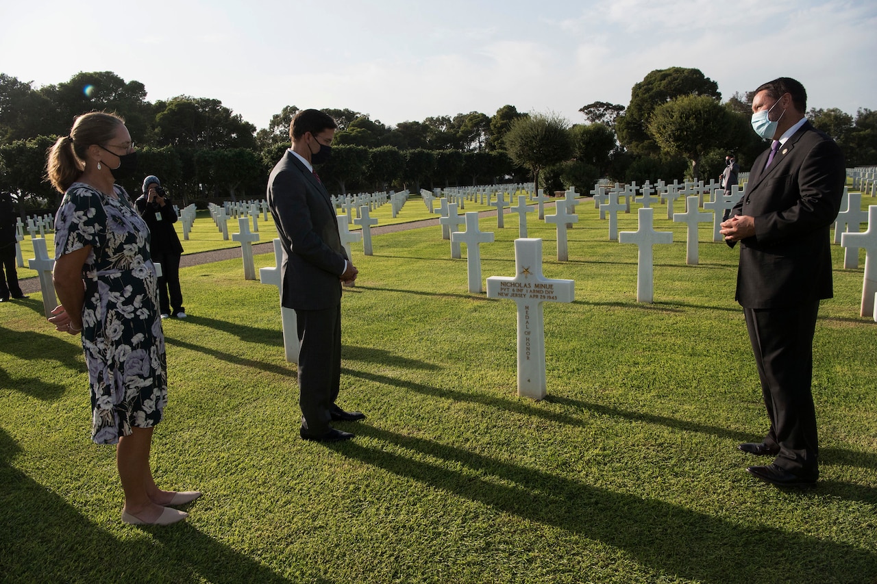 Several men and a woman stand beside a grave marker in a cemetery.