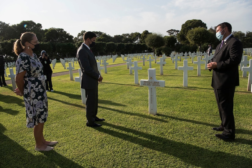 Several men and a woman stand beside a grave marker in a cemetery.