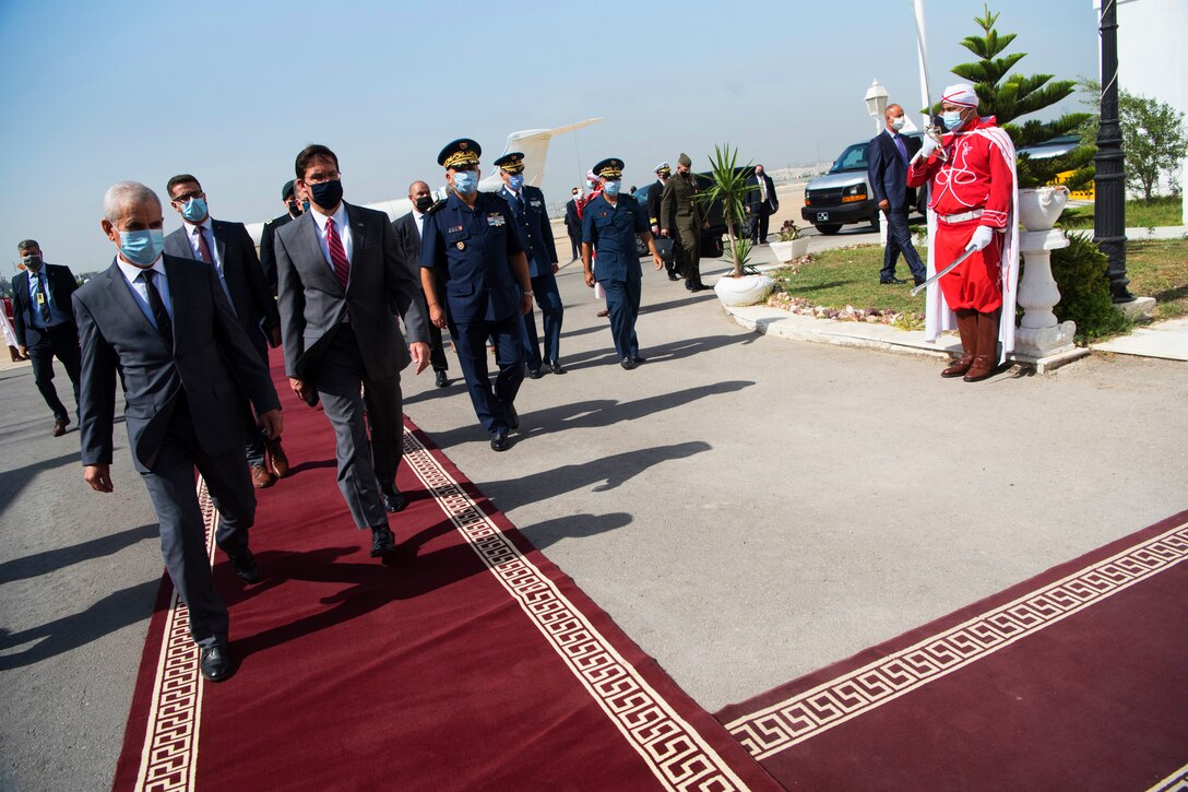 Defense Secretary Dr. Mark T. Esper walks with other officials on a red carpet outdoors.