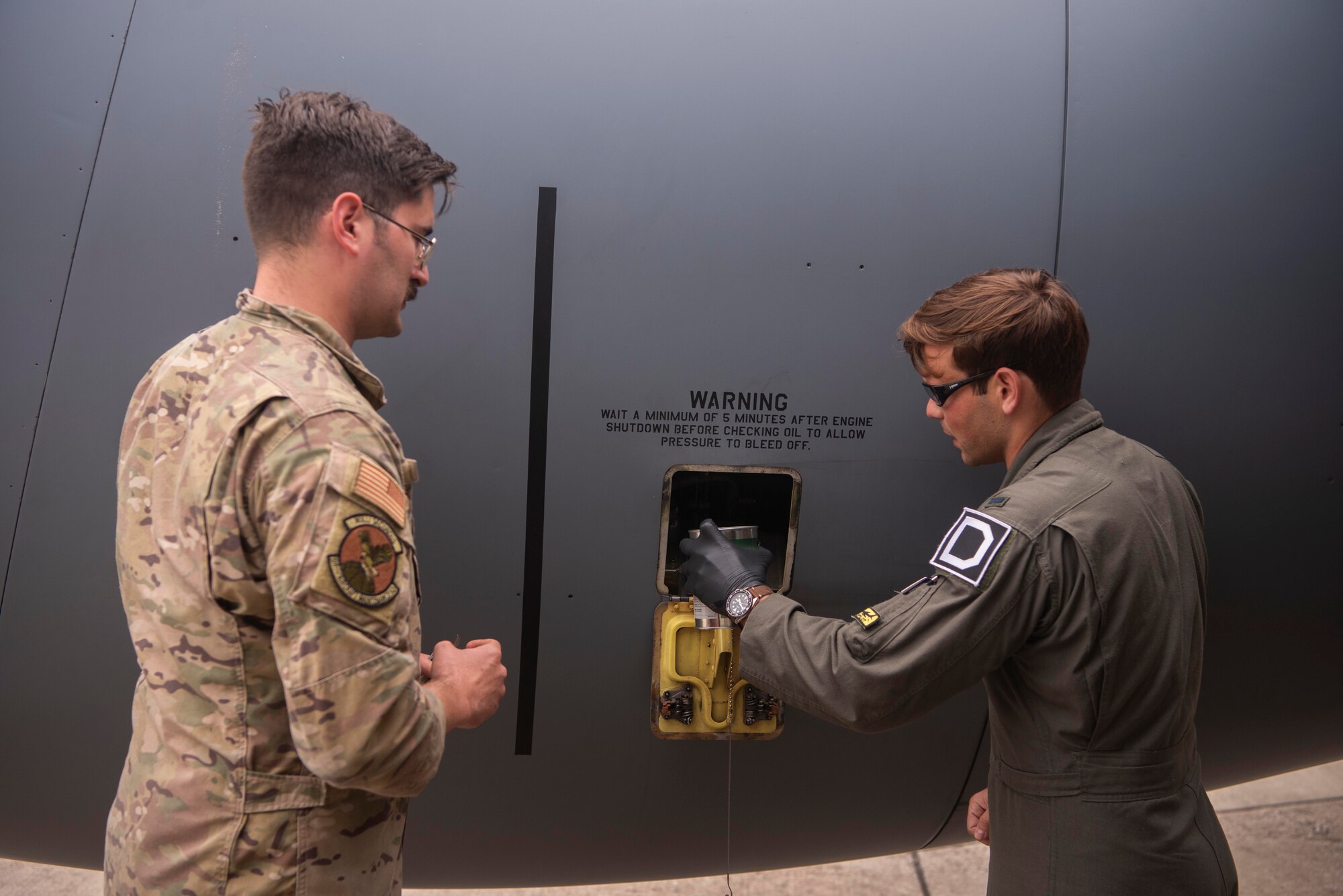 U.S. Air Force Staff Sgt. Lance Whisenhunt, 100th Aircraft Maintenance Squadron flying crew chief, left, oversees 1st Lt. Bradley Mokris, 351st Air Refueling Squadron pilot, service the oil of a  KC-135 Stratotanker aircraft during Exercise Wolff Pack at Royal Air Force Mildenhall, England, Sept. 30, 2020. The exercise developed multi-capable Airmen who can accomplish duties outside of their typical responsibilities in support of the mission. (U.S. Air Force photo by Airman 1st Class Joseph Barron)