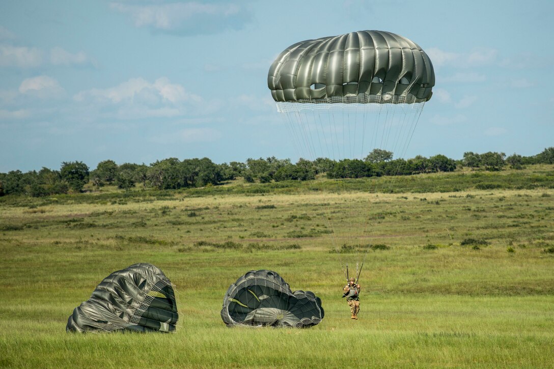 A paratrooper lands in a field where two other parachutes are on the ground.