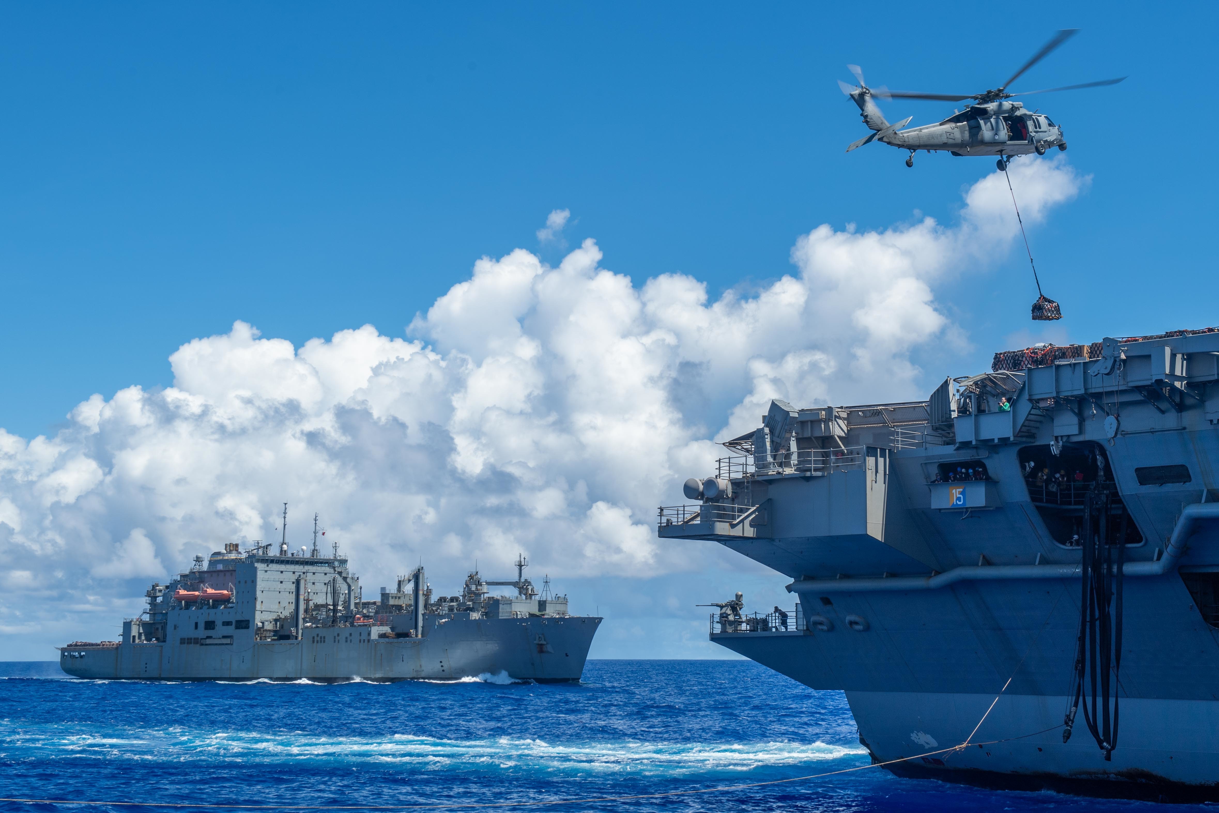 An MH-60S Sea Hawk, assigned to the "Golden Falcons" of Helicopter Sea Combat Squadron 12, carries cargo from the Lewis and Clark-class dry cargo and ammunition ship USNS Alan Shepard (T-AKE 3) to the Nimitz-class aircraft carrier USS Ronald Reagan (CVN 76) while conducting vertical replenishments (VERTREP).