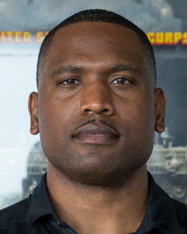 A Marine wearing a polo-style shirt with a Marine Corps recruiting station logo on it stands for a photo.