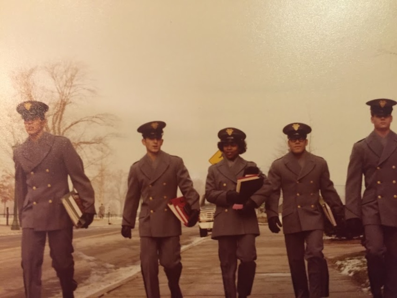 A group of 5 soldiers holding books walk together.