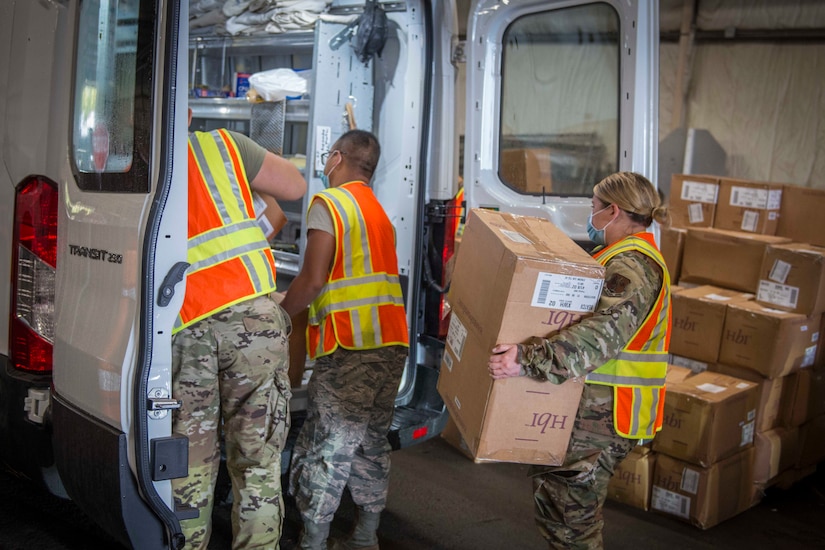 Airmen wearing face masks load boxes into a vehicle.