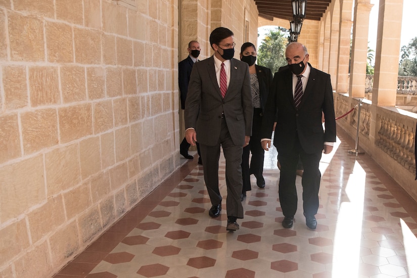 Two men, wearing masks, walk down a breezeway.