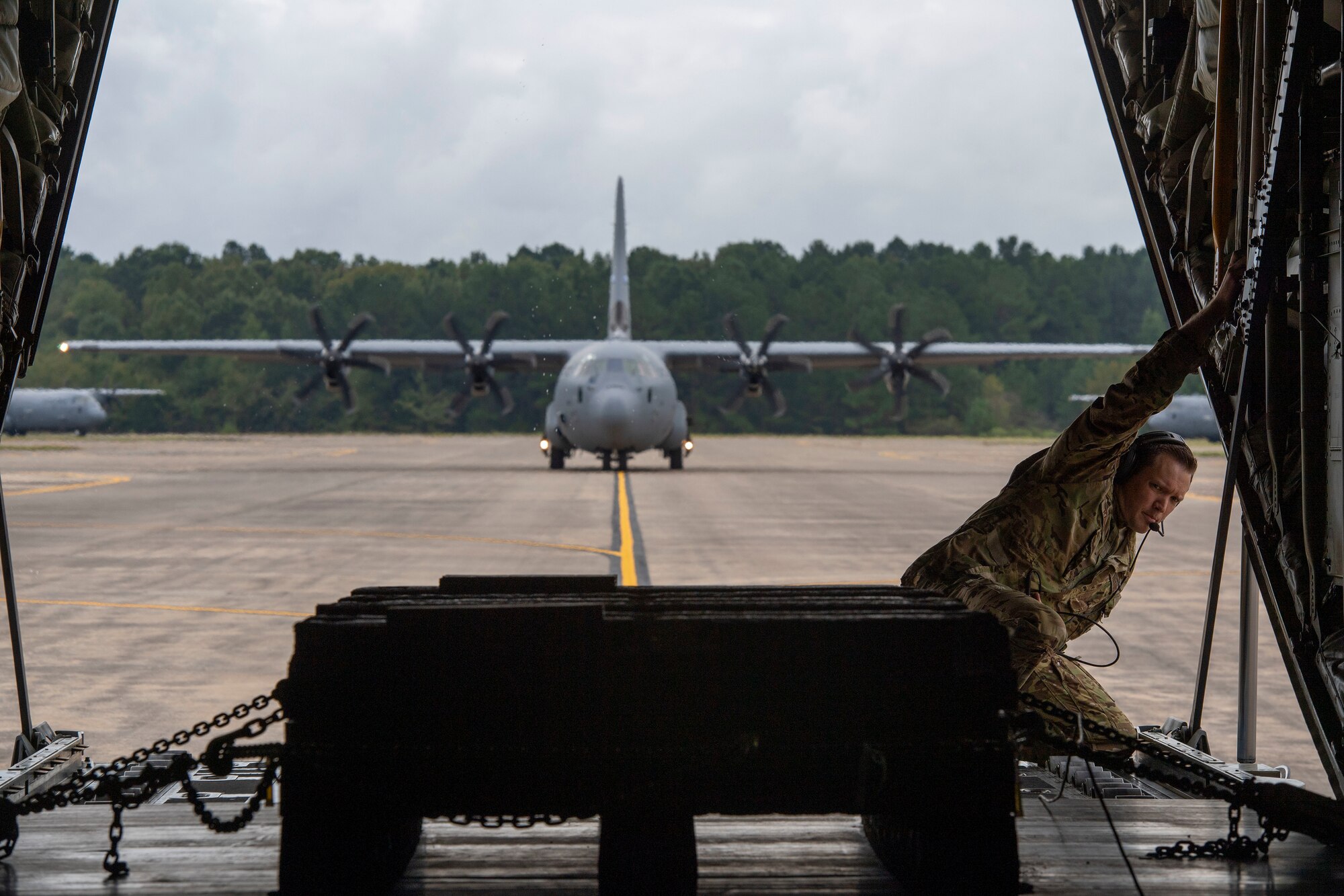 A loadmaster looks out the back of a C-130J.