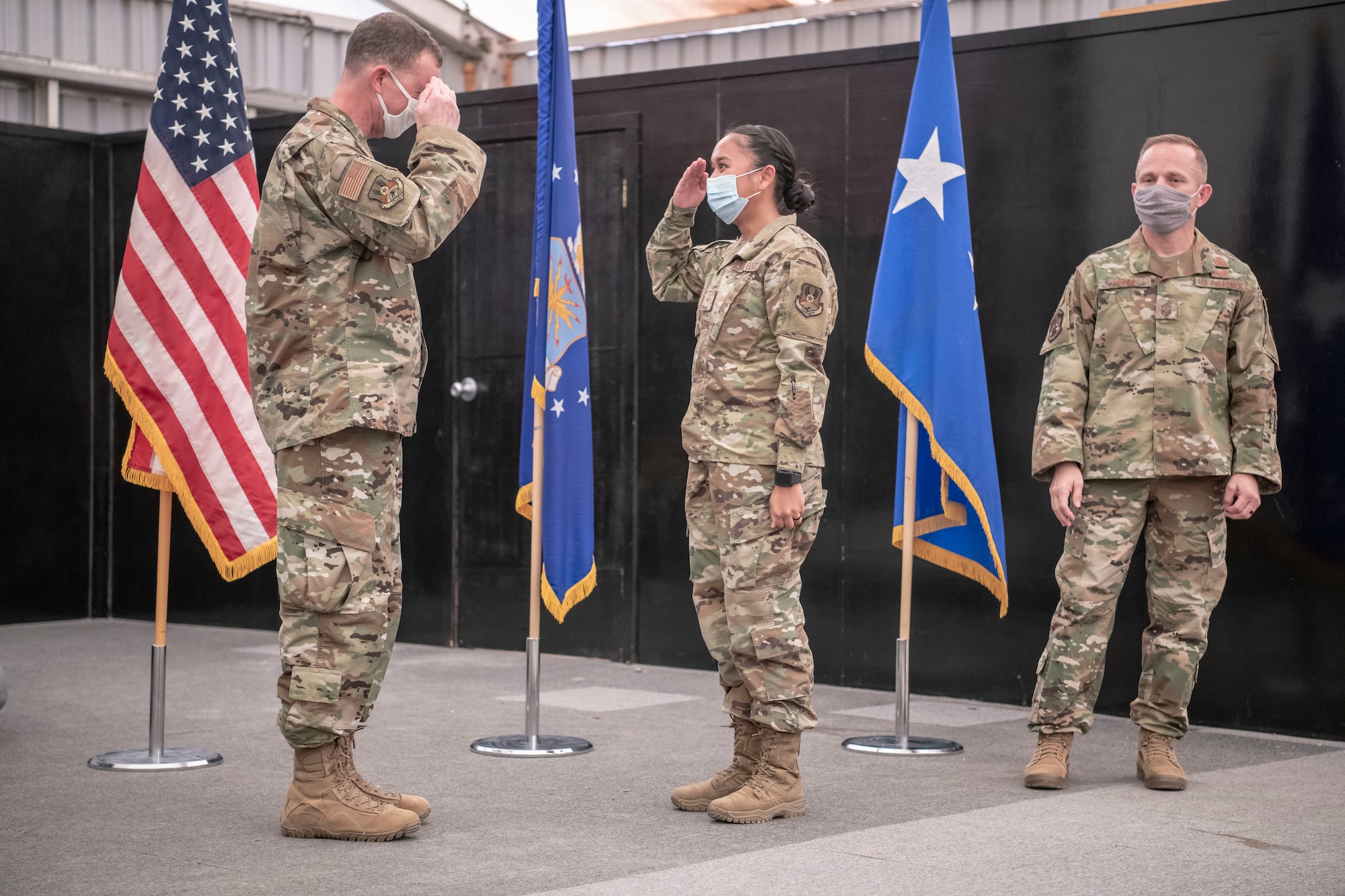 Lt. Gen. Greg Guillot, U.S. Air Forces Central commander, and Senior Airman Erika Louise Ramirez, 380th Expeditionary Medical Group, render a salute during a coining ceremony as Chief Master Sgt. John Storms, U.S. Air Forces Central command chief, observes during an all-call at Al Dhafra Air Base, United Arab Emirates, Sept. 27, 2020