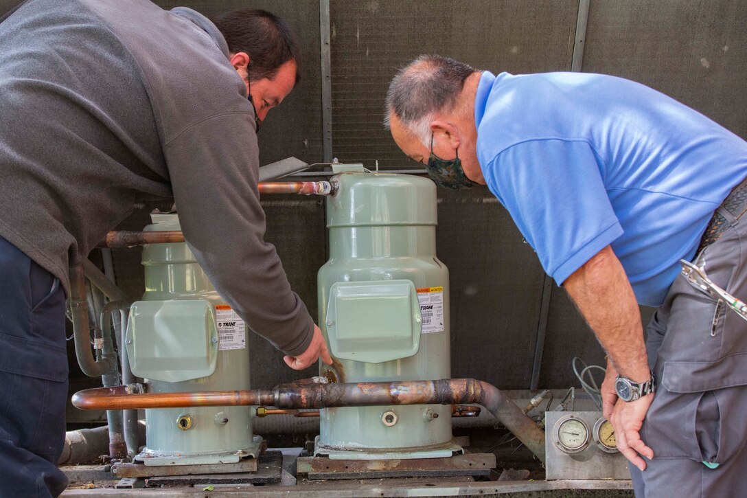 Members of Headquarters and Service Battalion, U.S. Marine Corps Forces Command, Fleet Marine Force Atlantic, Facility Maintenance Team, Abraham Egley, left, and Terrance Henry, inspect the pipes for a heating, ventilation, and air conditioning system (HVAC) May 13, 2020, at Hopkins Hall Gym, on Camp Elmore in Norfolk, Virginia.