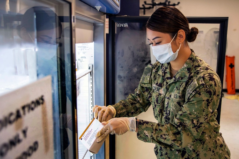 A Navy seaman wearing a face mask and gloves prepare vaccines.