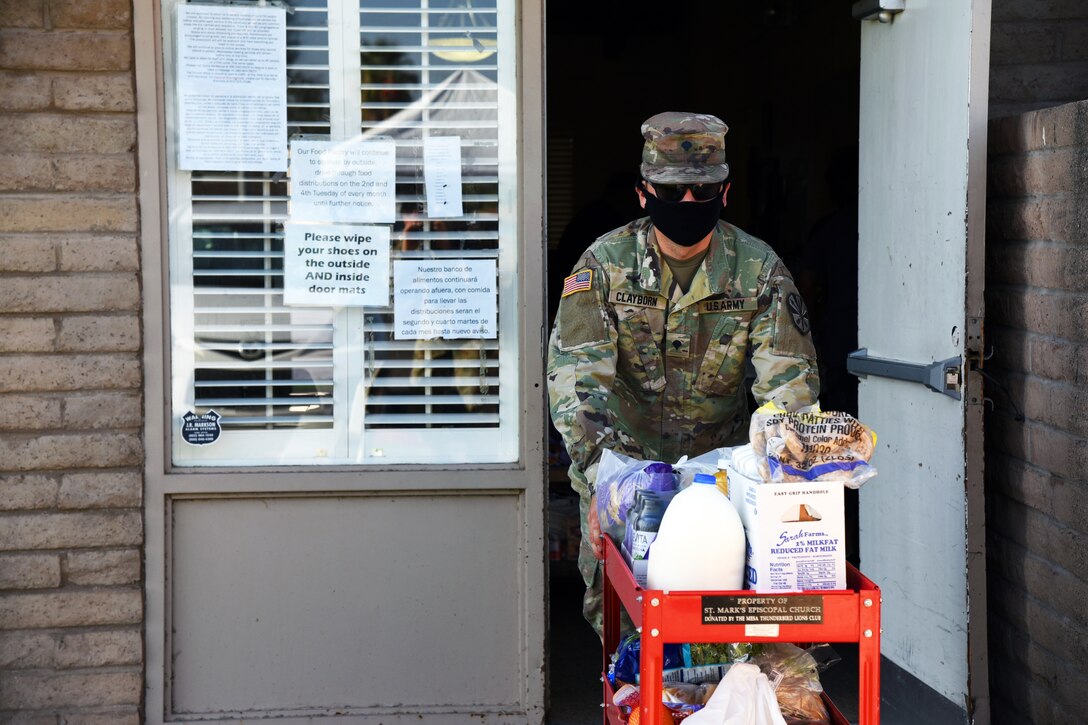 A National Guardsman wearing a face mask and gloves pushes a cart with groceries on it for residents at a local food bank.