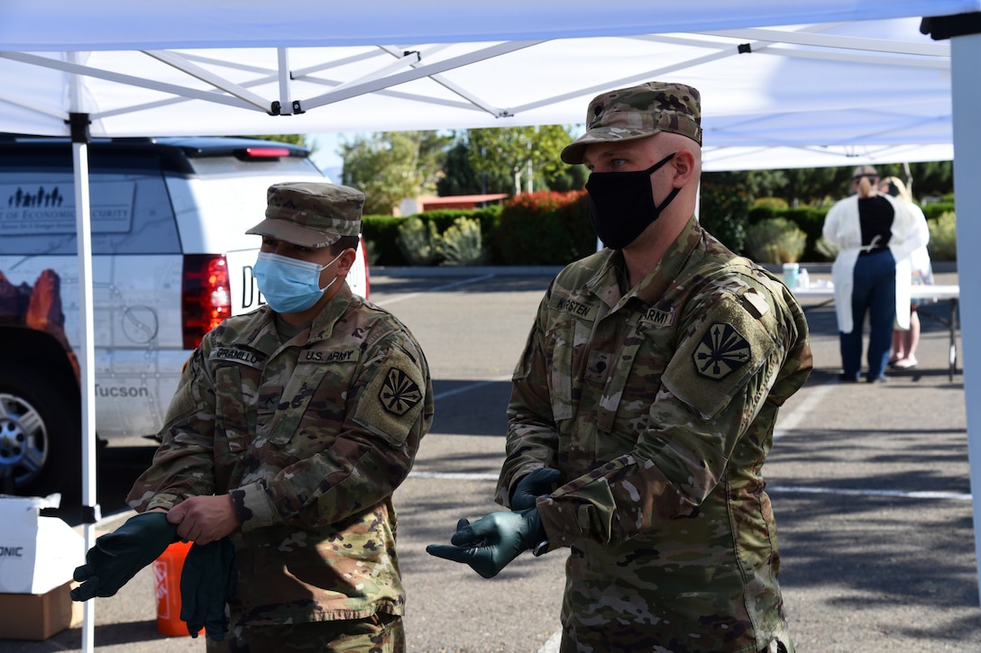 Two National Guardsmen wearing masks are putting on gloves to start collecting COVID-19 test samples.