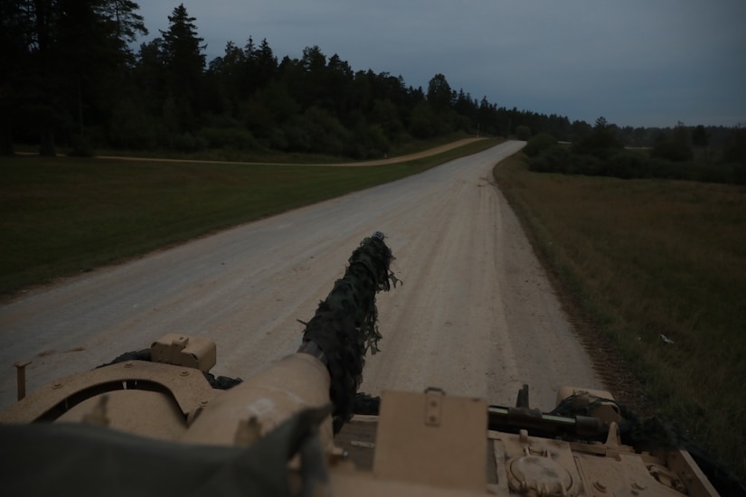 The view of a road and trees from inside a military vehicle.