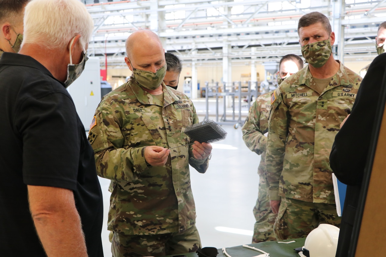 A man examines a long, thin piece of plastic as other men stand nearby; all are wearing face masks.