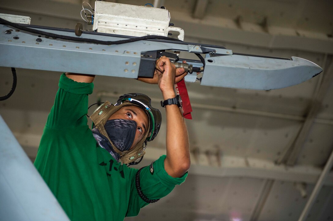 A sailor wearing a mask  works on an aircraft.