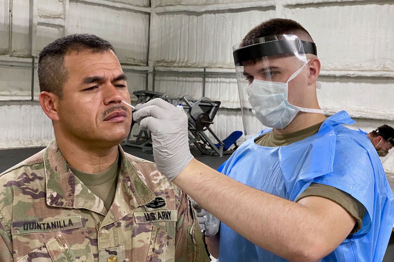 A man wearing PPE uses a nasal swab to obtain a COVID-19 test sample from a soldier.