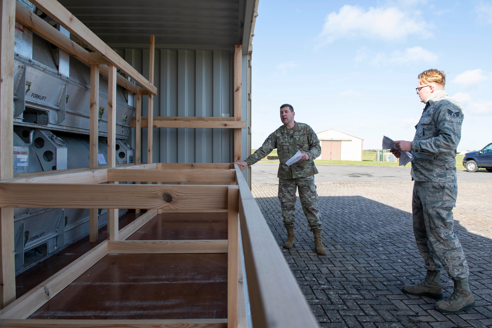 U.S. Air Force Senior Airman Ian Fike, right, 420th Munitions Squadron conventional maintenance crew chief, shows Col. Kurt Wendt, left, 501st Combat Support Wing commander, regulations and instructions to build wooden blocking and bracing to secure munitions during shipment, during a visit to RAF Welford, England, Oct. 1, 2020. Wendt visited 420th MUNS to meet with the Airmen and to learn more about their new mission capabilities. (U.S. Air Force photo by Senior Airman Jennifer Zima)