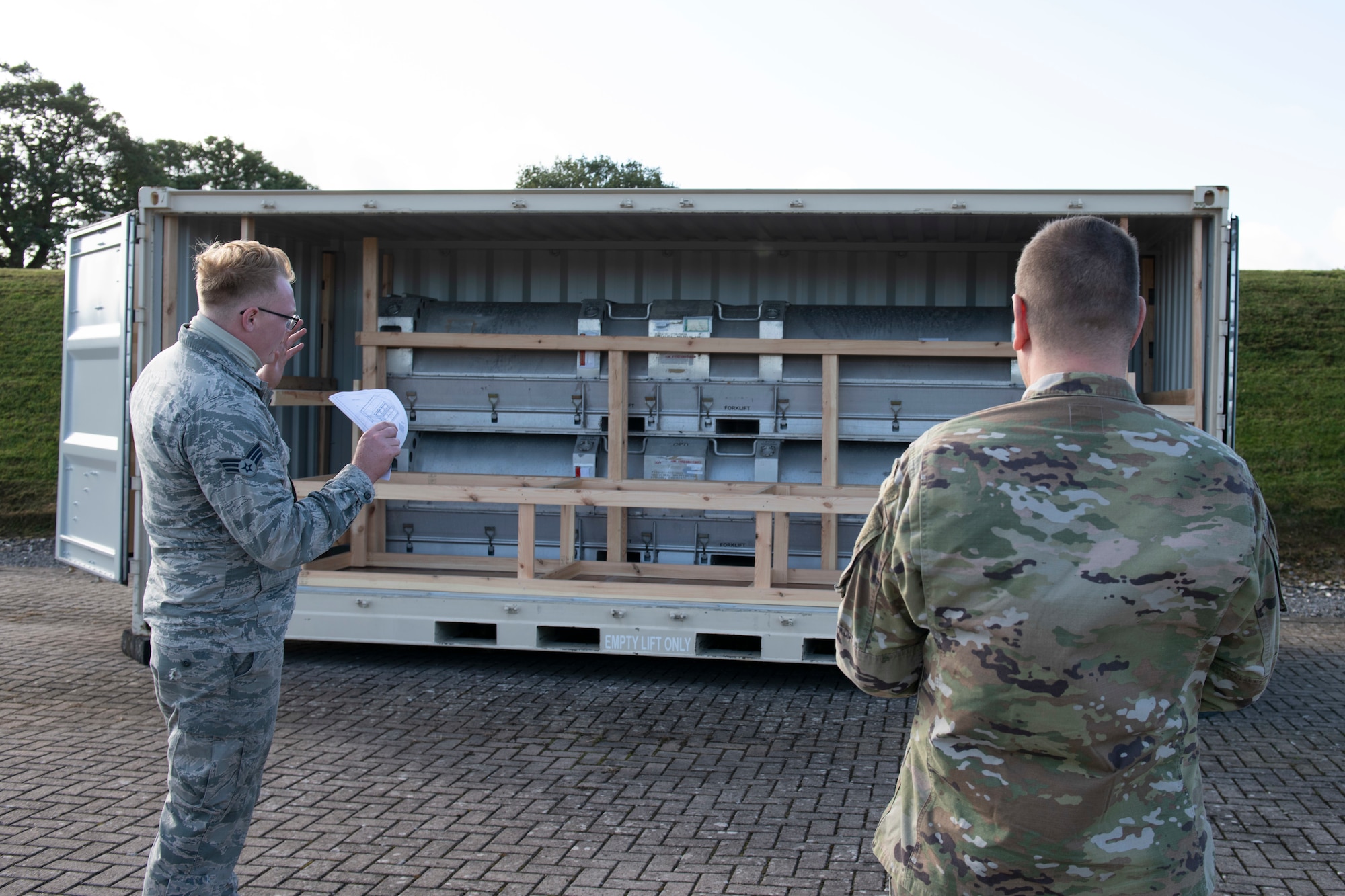 U.S. Air Force Senior Airman Ian Fike, left, 420th Munitions Squadron conventional maintenance crew chief, shows Col. Kurt Wendt, right, 501st Combat Support Wing commander, regulations and instructions to build wooden blocking and bracing to secure munitions during shipment, during a visit to RAF Welford, England, Oct. 1, 2020. Wendt visited 420th MUNS to meet with the Airmen and to learn more about their new mission capabilities. (U.S. Air Force photo by Senior Airman Jennifer Zima)