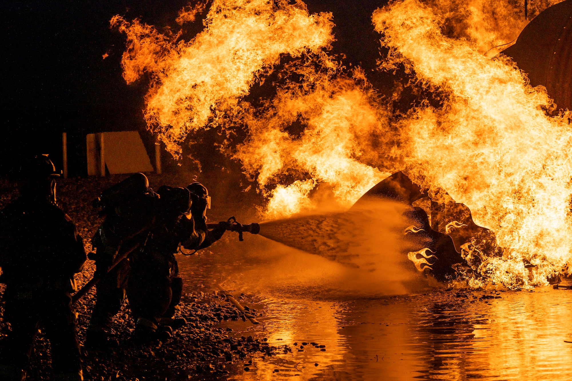 Firefighters from the 436th Civil Engineer Squadron and Magnolia Volunteer Fire Company Station 55, from Delaware, spray down an aircraft-fire trainer during a live-fire-burn exercise at night Sept. 28, 2020, on Dover Air Force Base, Delaware. Total Force and civilian fire companies in the surrounding community often partner with Dover AFB to complete annual training requirements. (U.S. Air Force photo by Senior Airman Christopher Quail)