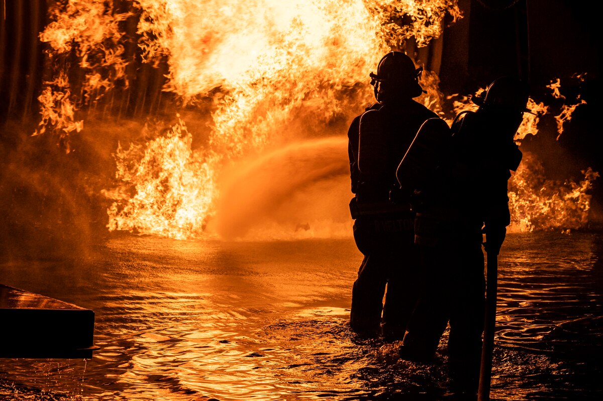 Firefighters from the 436th Civil Engineer Squadron and Magnolia Volunteer Fire Company Station 55, from Delaware, spray down an aircraft fire trainer during a live-fire-burn exercise at night Sept. 28, 2020, on Dover Air Force Base, Delaware. Temperatures inside the aircraft-fire trainer can reach up to 1,500 degrees Fahrenheit. (U.S. Air Force photo by Senior Airman Christopher Quail)