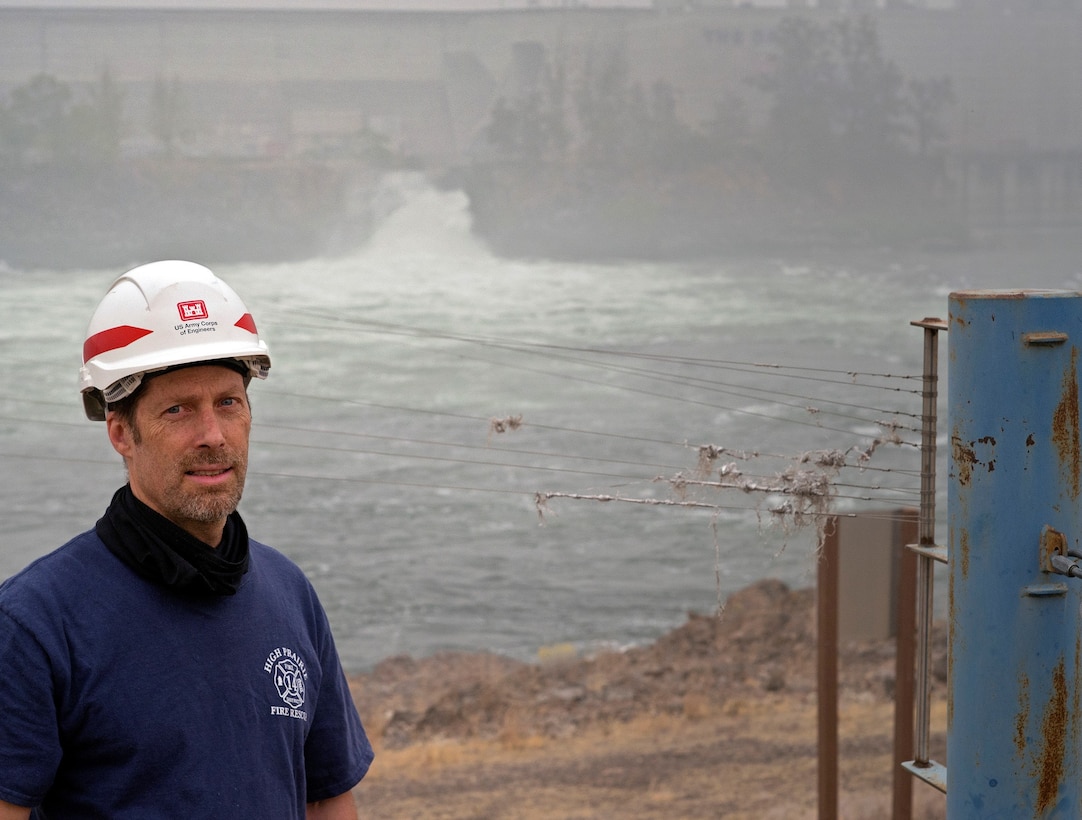 Jim Day, fisheries biological technician inspects avian wires at The Dalles Lock and Dam-seen in the background. The wires help deter birds from preying on juvenile salmon as they migrate downstream through the sluiceway.