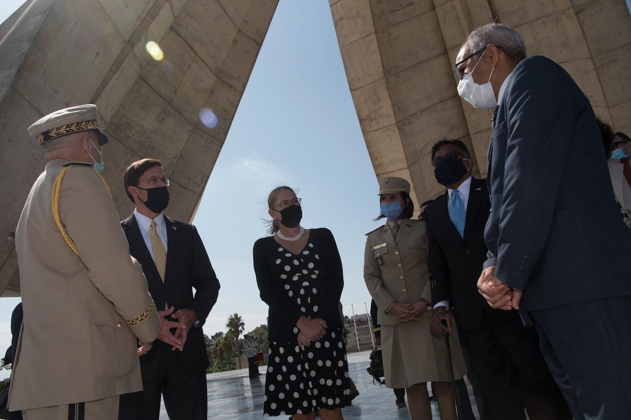 Men and women wearing face masks stand in a half circle while conversing.