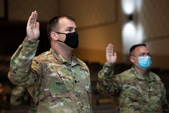 Air Force officers, assigned to Air University, raise their right hand and recite the Oath of Office during a ceremonial swear-in in Polifka Auditorium.
