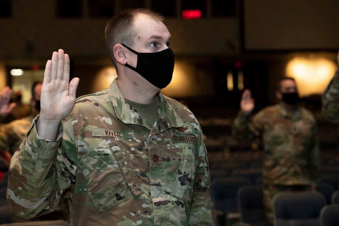 Air Force officers, assigned to Air University, raise their right hand and recite the Oath of Office during a ceremonial swear-in in Polifka Auditorium.