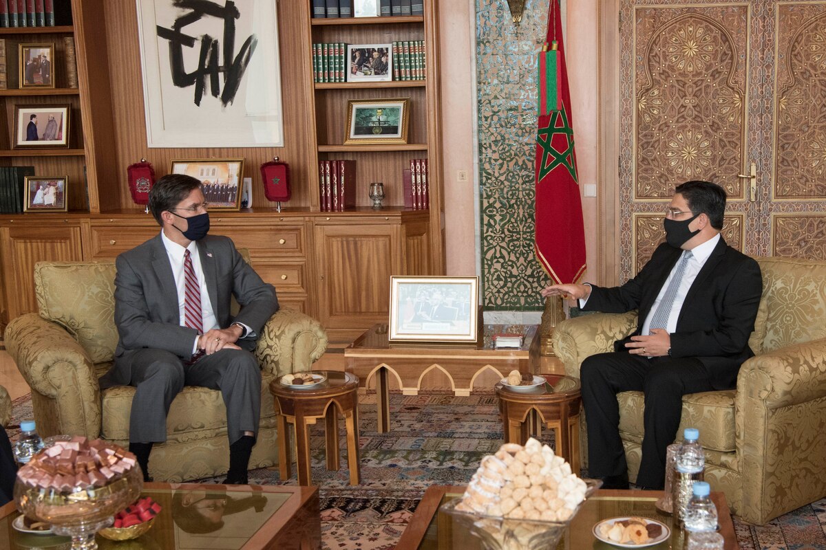 Two men wearing face masks, sitting in chairs, are turned to each other for a discussion.
