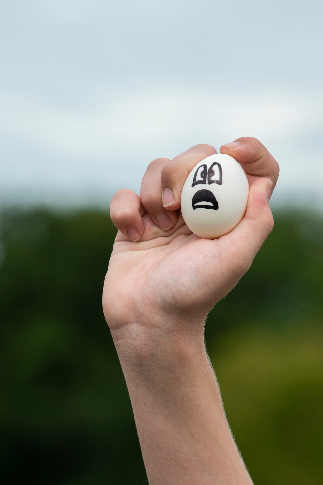 Photo of young hand holding an egg with expression drawn on it.