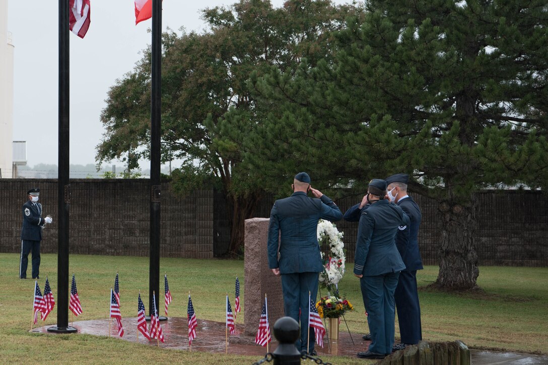 Three men saluting, facing wreath of flowers