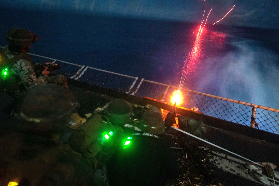 Marines and sailors fire a machine gun from a ship at night.