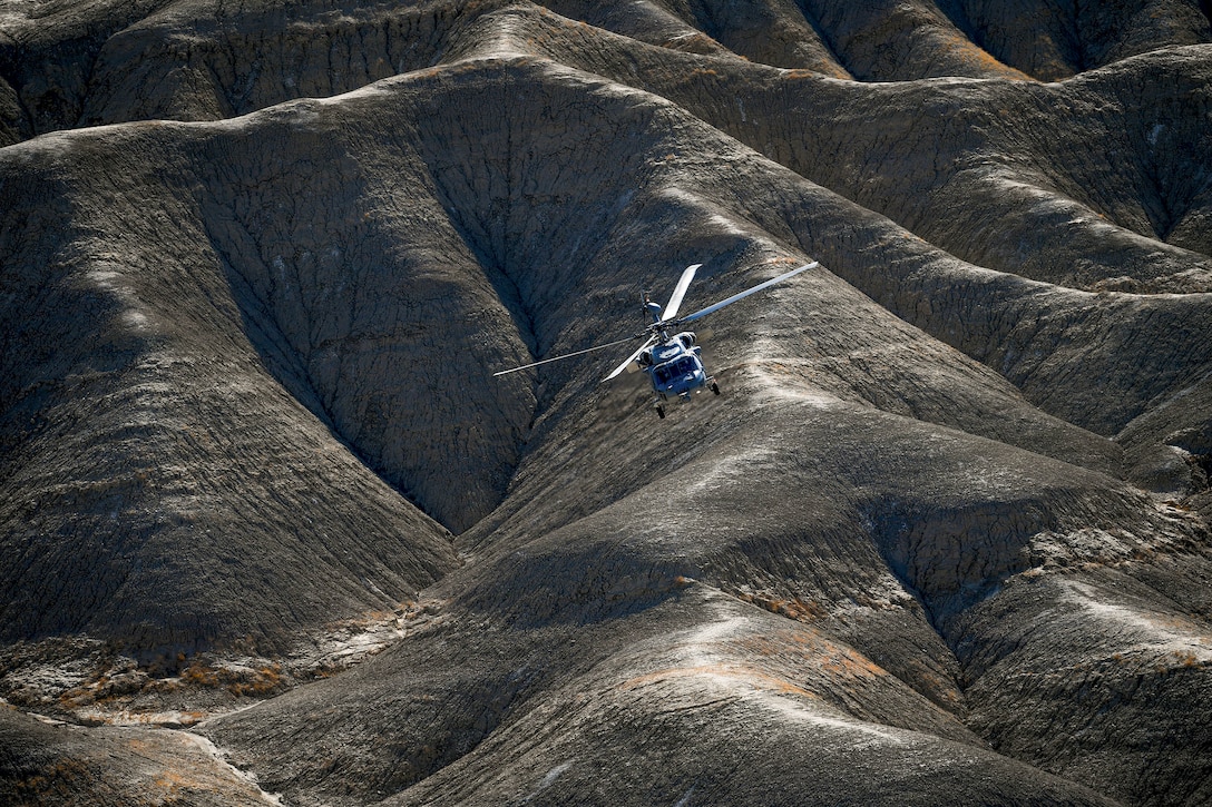 A Navy helicopter flies low over brown foothills.