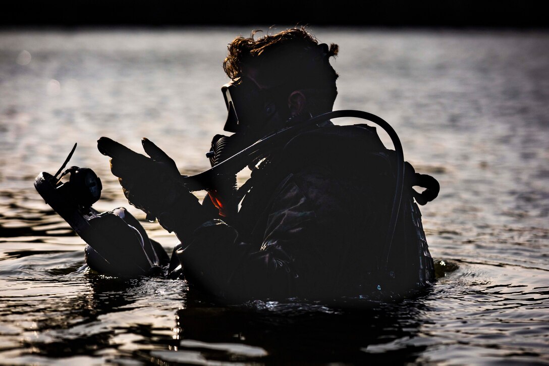 A Marine wearing dive gear moves in shoulder-deep water.