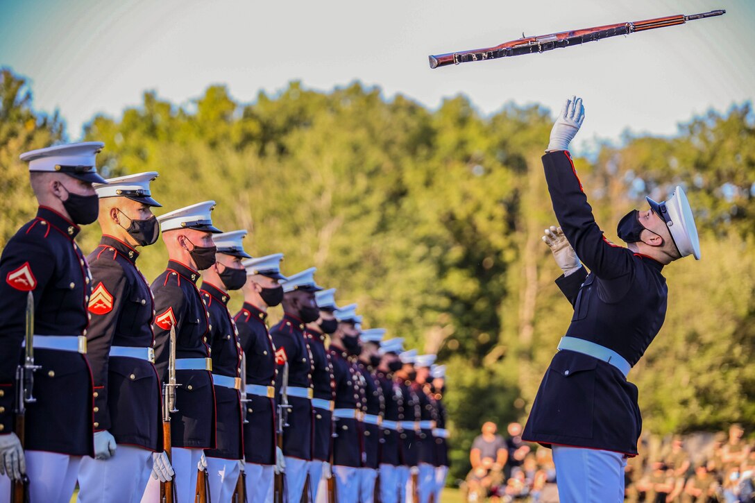 Marines stand in a row as another Marine throws a rifle in the air.