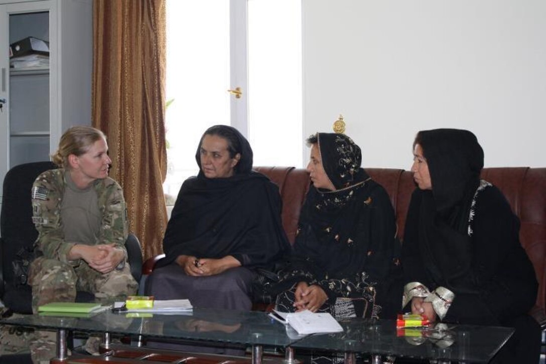 Three women in black robes sit on a couch and talk to a woman in a military uniform who is sitting on a chair.