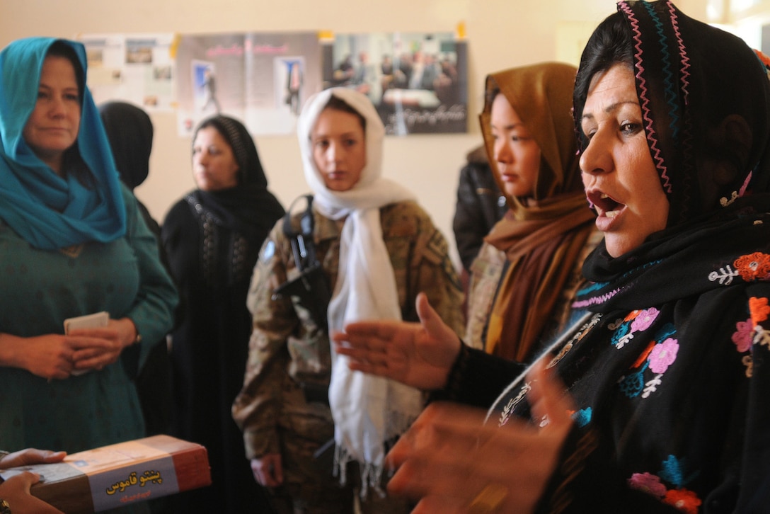 Women in headscarves stand together, indoors, and speak with each other.