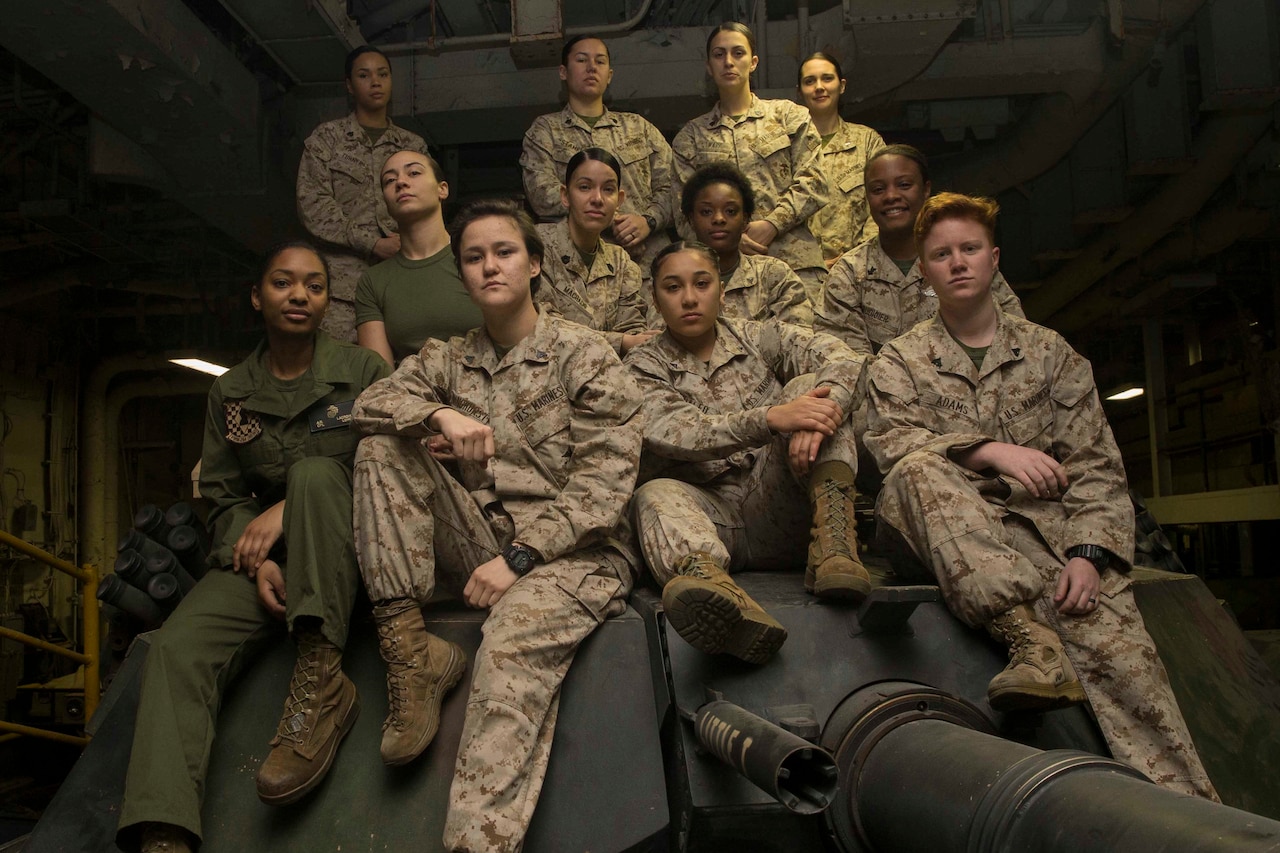 A dozen women in military uniforms sit on a tank turret.