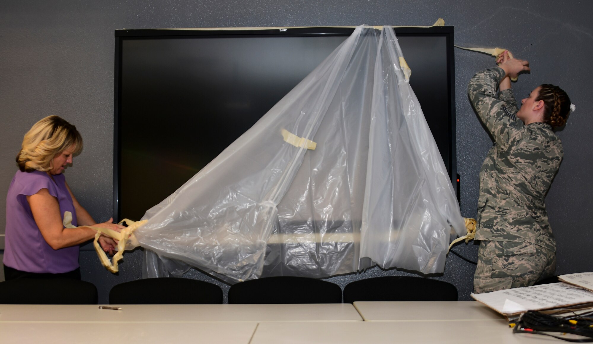 A photo of an Airman and a civilian taking a sheet of plastic down off the new SmartBoard in the EO conference room.