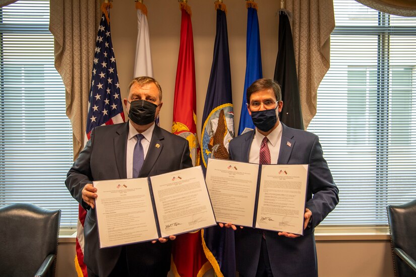 Two men hold two government documents as they pose for a photo.