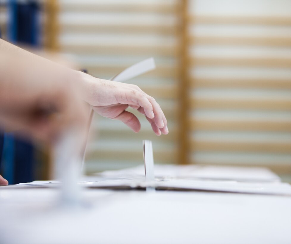 Hand is putting a ballot into a voting box.